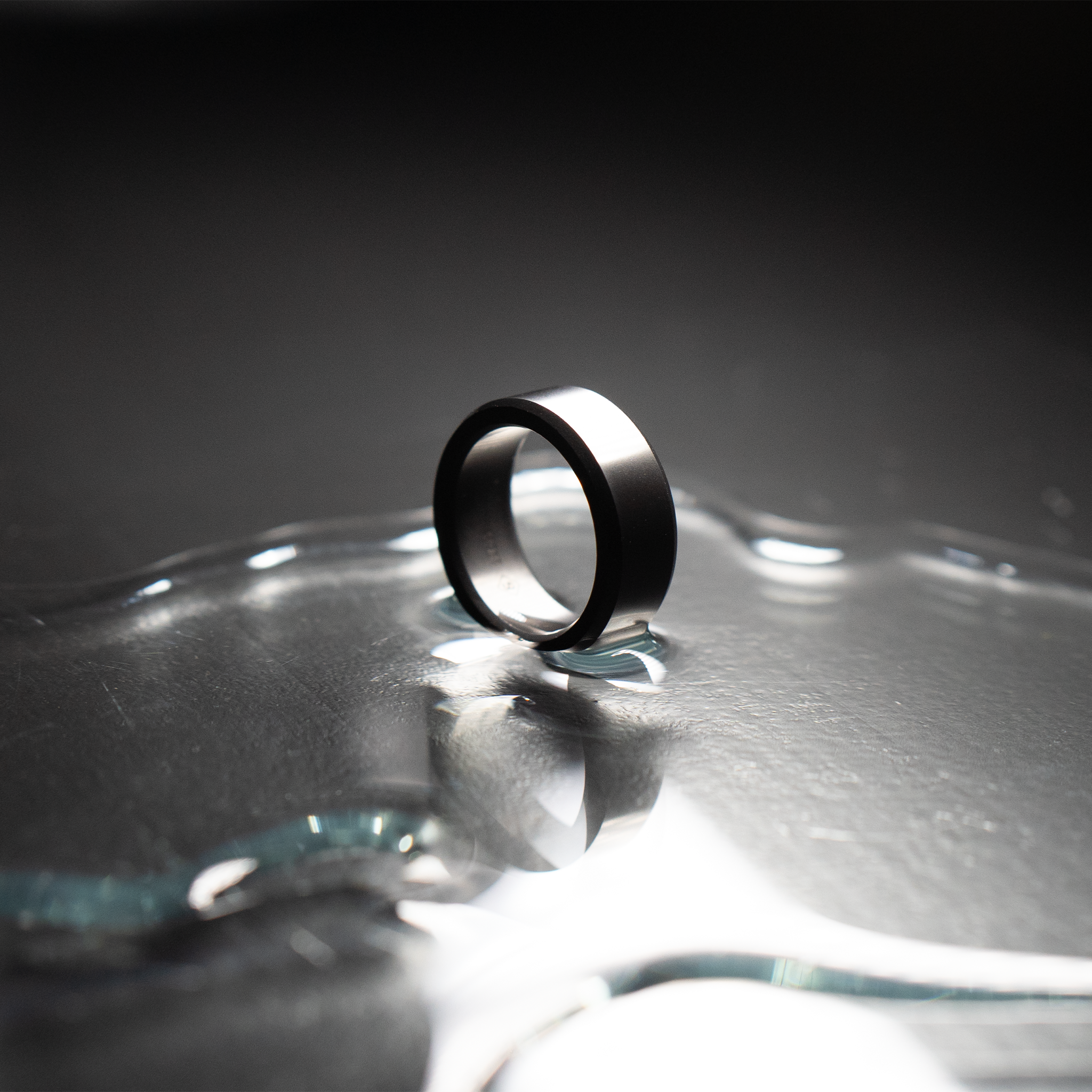 Image of beveled, polished Elysium Black Diamond ring resting in water on a black surface