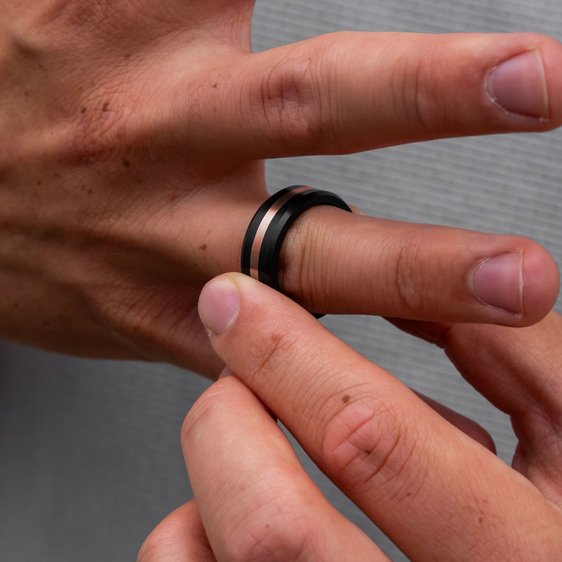 Lifestyle shot #3 of men's hands wearing our Elysium ARES Men's Black Diamond & 18k Rose Gold Inlay | ElysiumBlack.com | Men’s 18k Rose Gold Inlay Wedding Rings