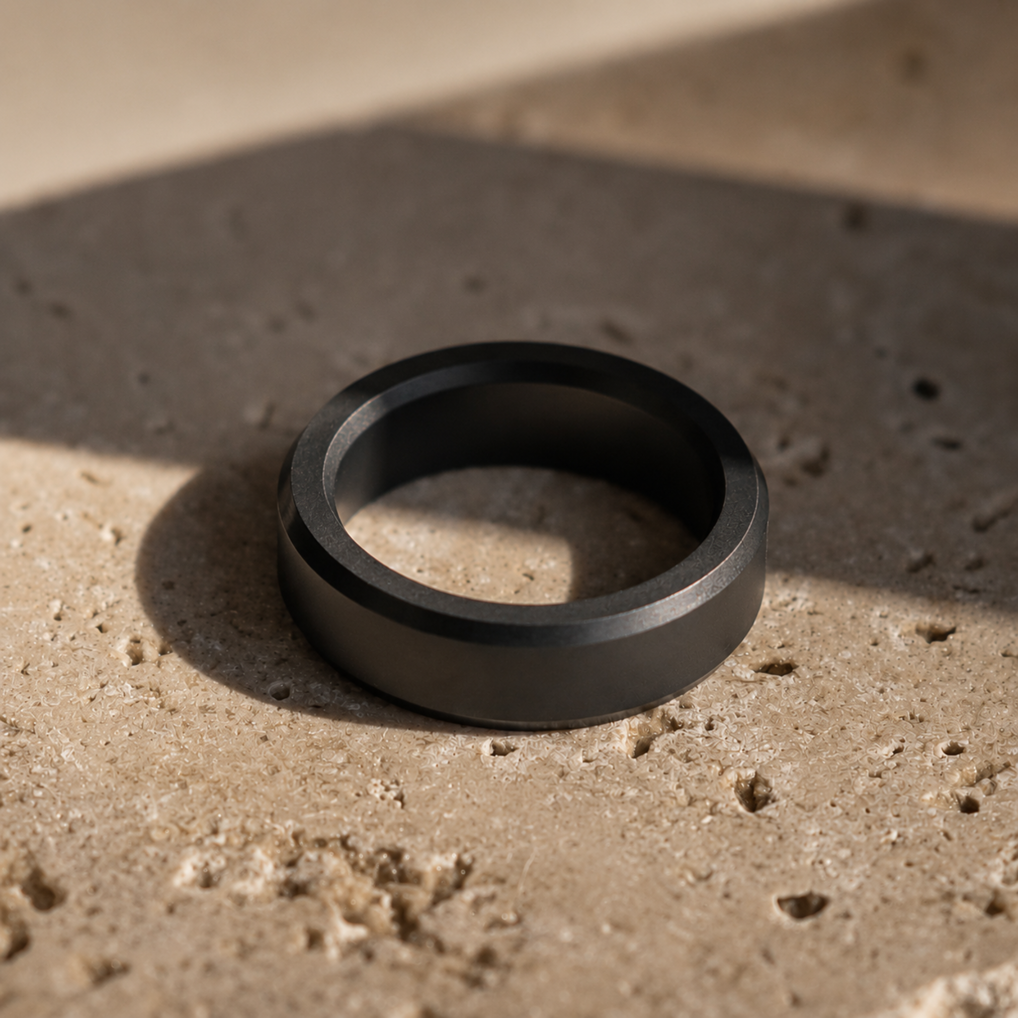 ARES solid black diamond wedding band in 6mm polished finish, displayed on a stone surface in a refined editorial setting.