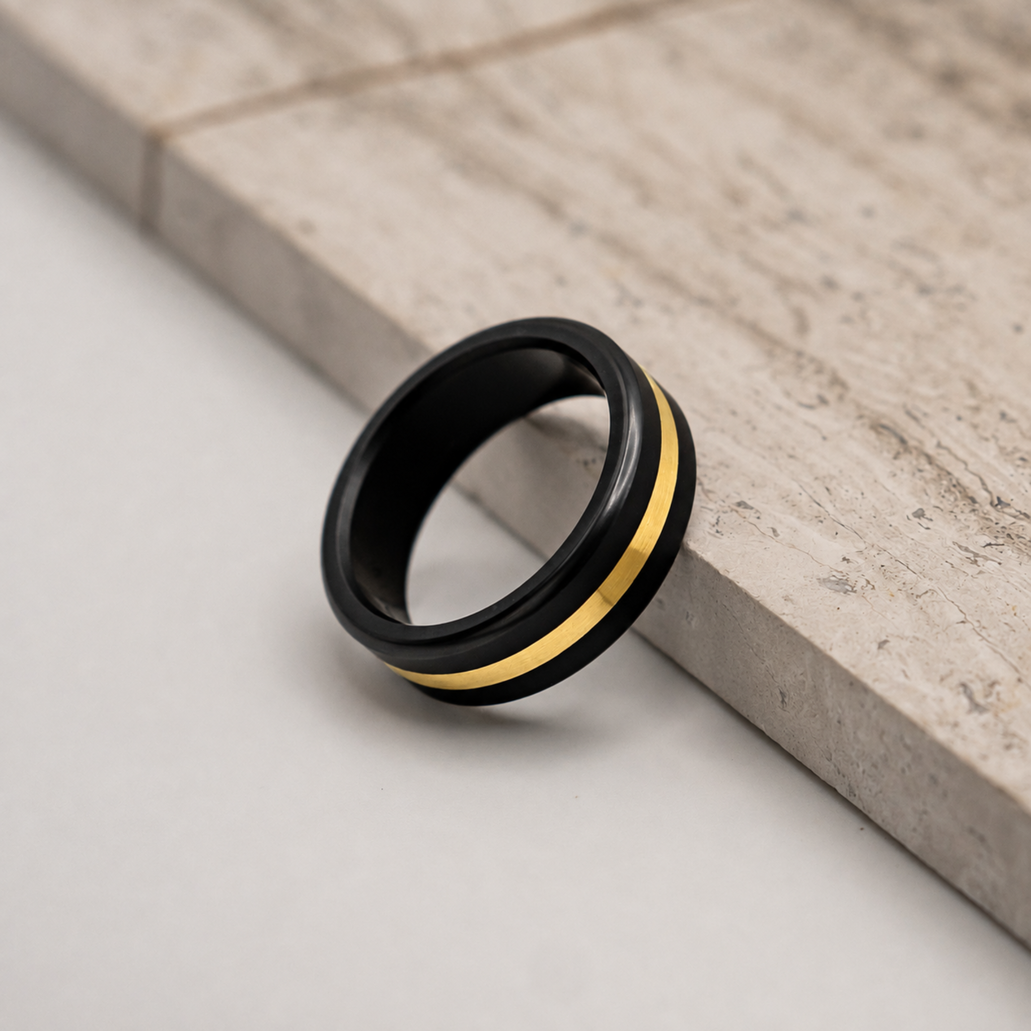 ARES 8mm solid black diamond ring with 24K yellow gold inlay on a stone surface